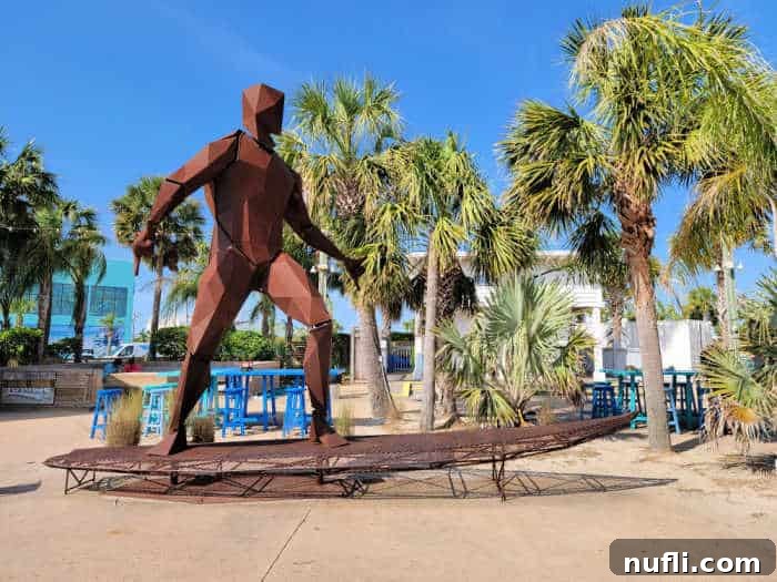 Large metal surfer statue on a metal surfboard next to palm trees