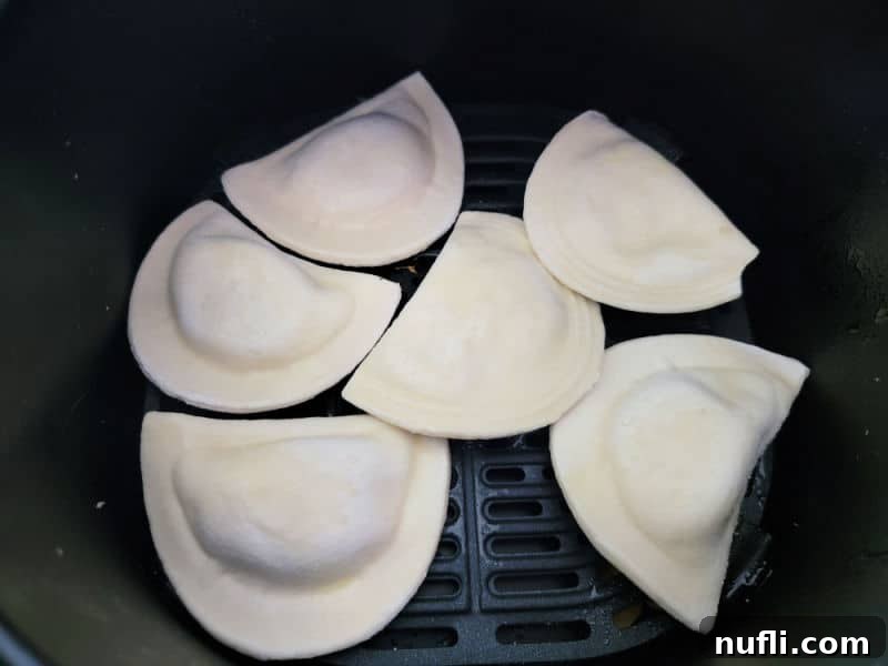 Crispy Air-Fried Pierogies 4 Several frozen pierogies arranged in a single layer in an air fryer basket, ready for cooking.