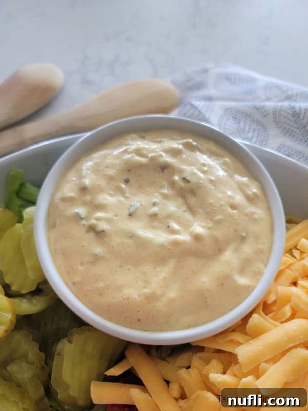 Big Mac Sauce in a white bowl next to pickles and shredded cheese