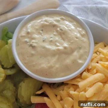 big mac sauce in a white bowl next to pickles and shredded cheese