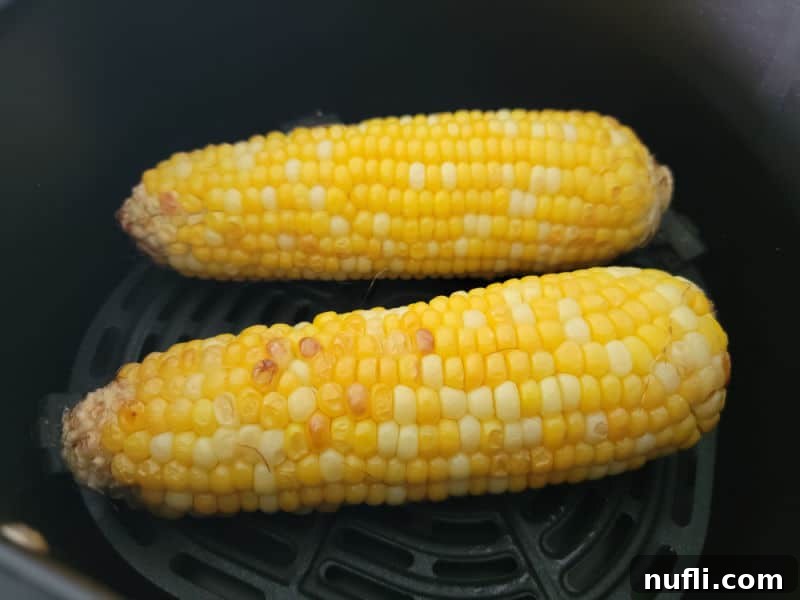 Two pieces of air fryer corn on the cob sitting in an air fryer basket