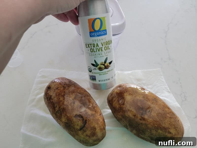 olive oil spray held next to two potato on a napkin