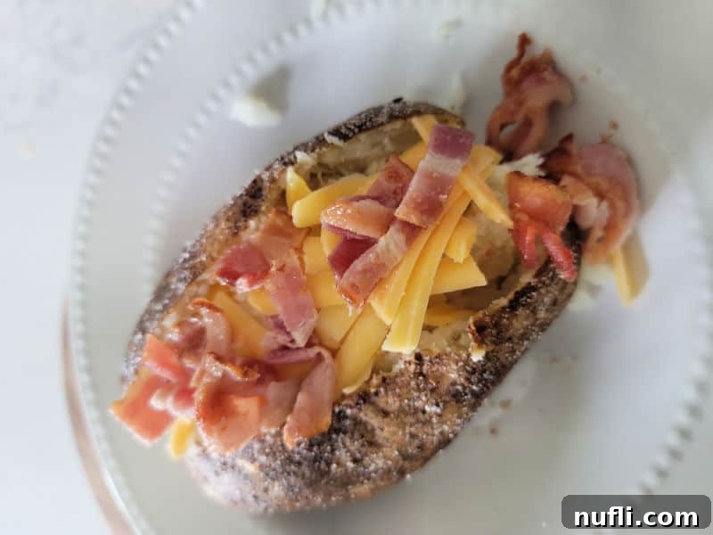 bacon and shredded cheddar cheese on a baked potato on a white plate