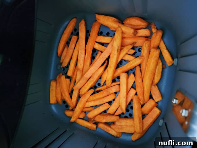 Sweet potato fries in an air fryer basket, perfectly cooked and golden brown