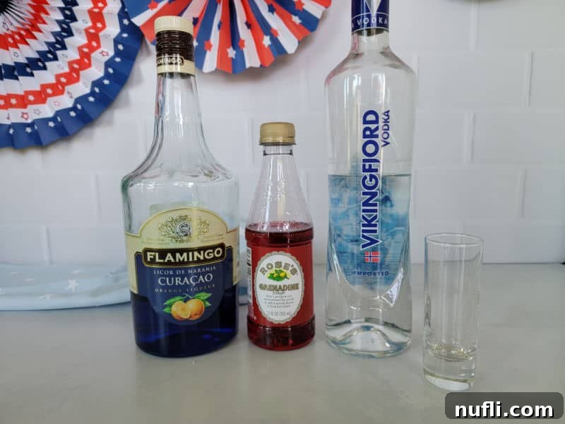 Ingredients for a patriotic shot including blue curacao, grenadine, vodka, and a shot glass, set against red, white, and blue decorations.