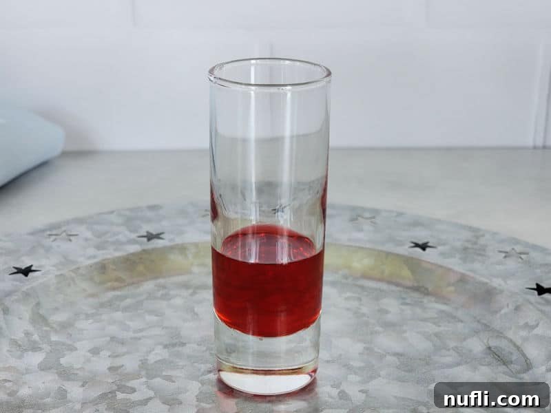 Red liquid carefully poured into the bottom of a shot glass, the first layer of a patriotic drink.