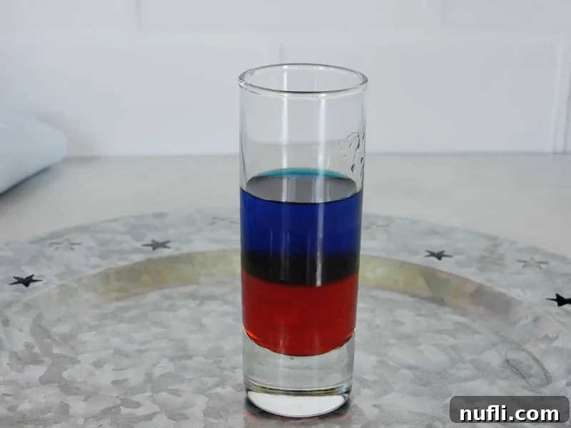 The first two layers of a red, white, and blue shot complete, showing red grenadine topped with a clear layer of blue curacao.