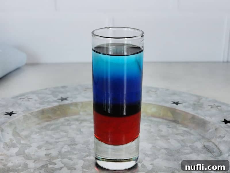 A completed red, white, and blue shot sitting on a silver platter with star decorations, showcasing all three vibrant layers.