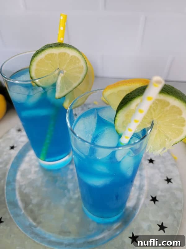 Two electric lemonade cocktails in tall glasses with paper straws and lemon and lime wheels for garnish