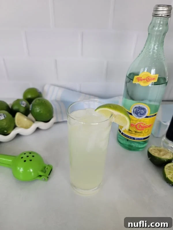 Ranch Water cocktail in a tall glass with al lime wedge, Topo Chico , limes, and lime squeezer