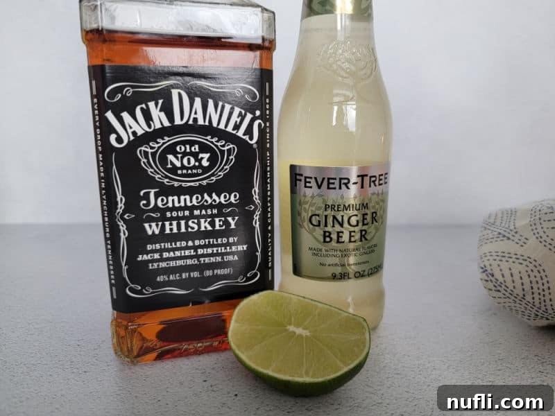 Jack Daniels Bottle, Ginger Beer bottle, half a lime on a counter with a fabric napkin