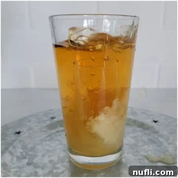 Glass shot dropping into a tall glass with brown orange liquid
