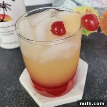 Malibu sunset drink in a clear glass garnished with maraschino cherries and pineapple chunk