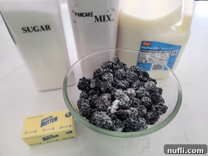Ingredients for Bisquick Blackberry Cobbler: blackberries in sugar, butter, Bisquick mix, and milk on a counter.