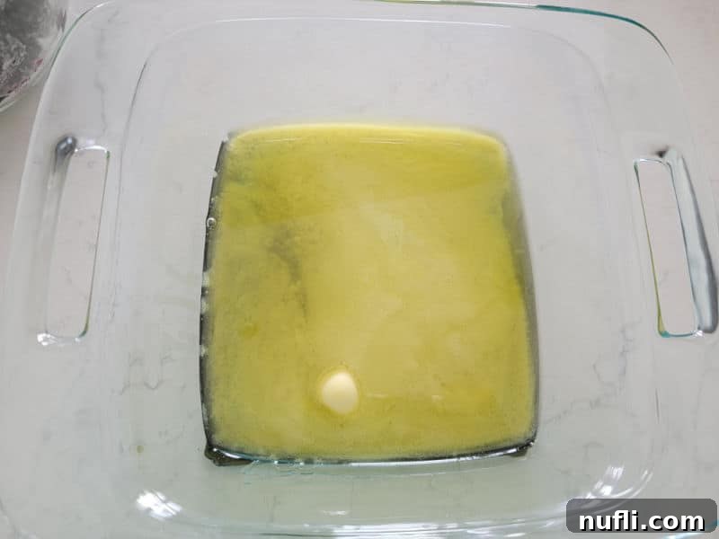 Melted butter in a clear glass 8x8 baking dish, ready for the cobbler batter.