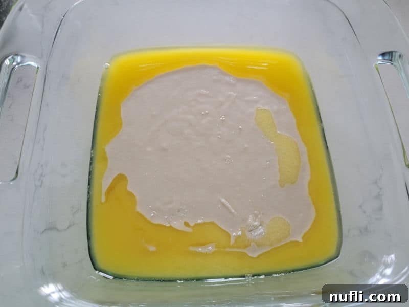 Bisquick baking mix poured over melted butter in a glass baking dish, not yet mixed.