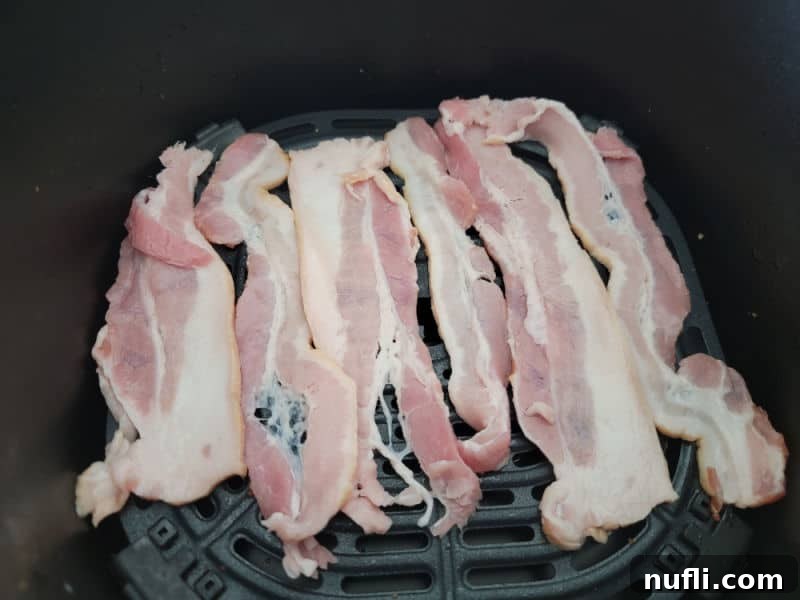 uncooked bacon spread on an air fryer basket