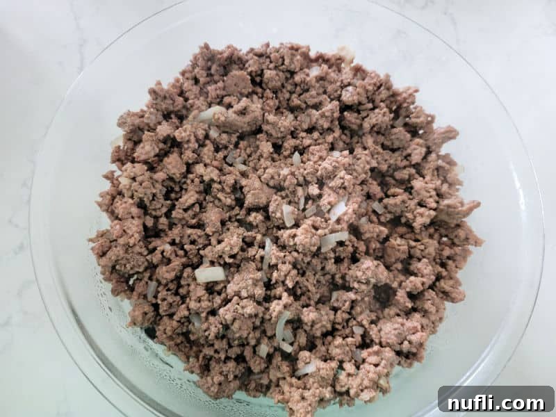 Ground beef and onion in a glass bowl for Bisquick impossible cheeseburger pie
