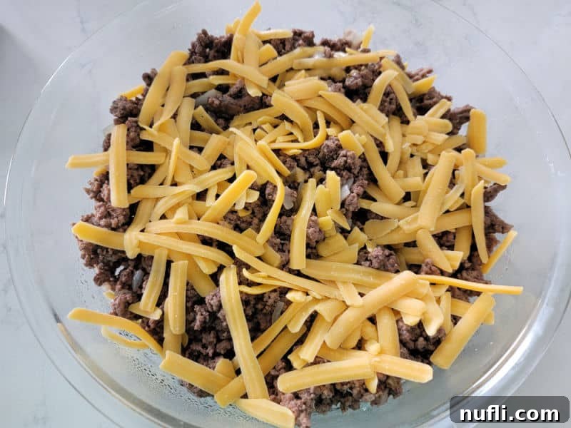 Shredded cheddar cheese on ground beef for Impossible Cheeseburger Pie Bisquick