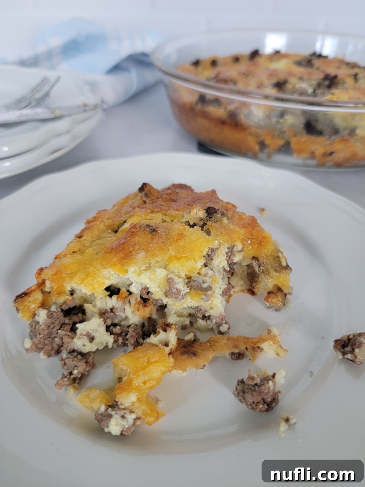 Slice of impossible pie on a white plate with the baking dish behind it and a pile of plates