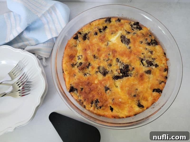 Impossible cheeseburger pie in a glass pie dish next to a stack of white plates and forks