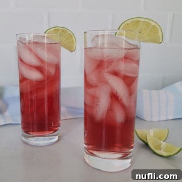 Effortless 3-Ingredient Woo Woo Cocktail 6 Two red Woo Woo Drinks in tall glasses with lime wedges next to a cloth napkin