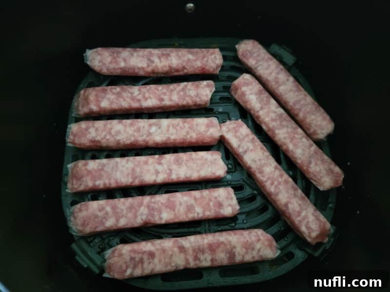 Crispy Air Fryer Sausages 4 Raw, uncooked breakfast sausage links arranged in a single, uncrowded layer within an air fryer basket, ready for cooking.