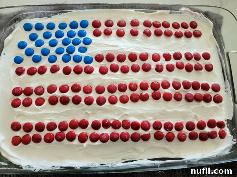 A patriotic poke cake in a glass baking dish, frosted with white topping and decorated with an American flag design using red and blue M&Ms.