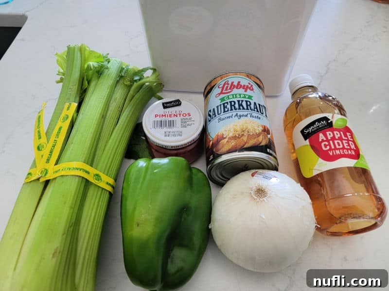 Simple and Delicious Sauerkraut Salad 3 Various Sauerkraut salad ingredients displayed on a kitchen counter: crisp celery, vibrant pimentos, green bell pepper, white onion, a jar of sauerkraut, and a bottle of apple cider vinegar.