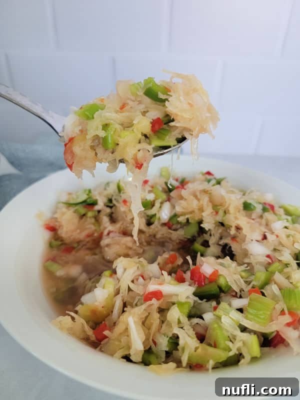Simple and Delicious Sauerkraut Salad 5 A serving spoon lifting a generous portion of homemade Sauerkraut salad from a white bowl, showcasing its colorful ingredients and inviting texture.