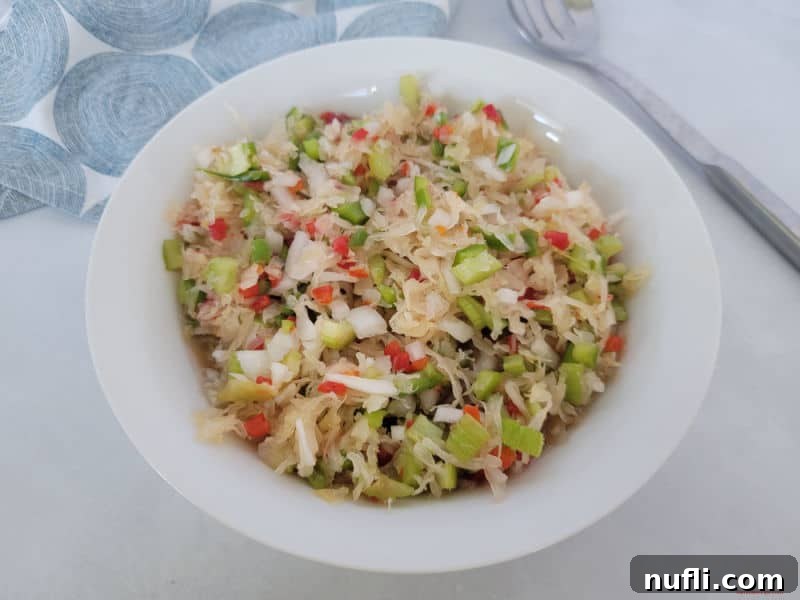 Simple and Delicious Sauerkraut Salad 6 A bowl of vibrant Sauerkraut salad positioned next to a neatly folded cloth napkin and a large serving spoon, ready for a meal.