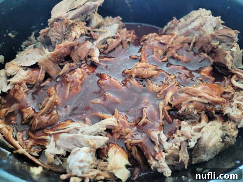 Pulled pork covered in barbecue sauce in a dark slow cooker bowl 