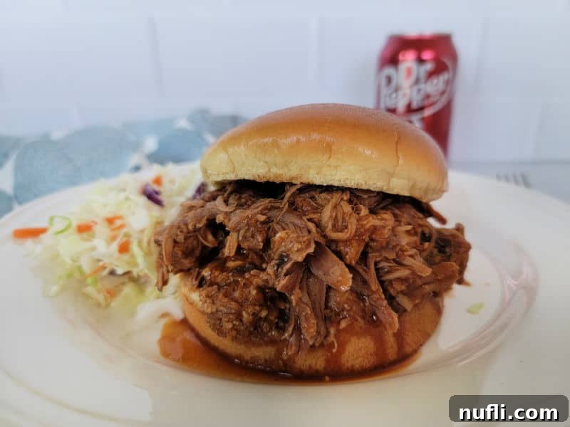 Pulled pork sandwich on a white plate with cole slaw near a can of Dr. Pepper 