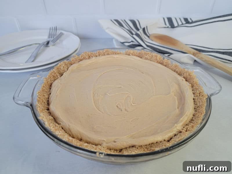 peanut butter pie in a graham cracker crust in a glass baking dish on a white counter with plates and forks in the background. 