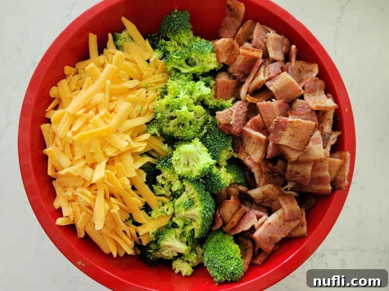 Loaded Broccoli Bacon Salad 3 Shredded cheddar cheese, broccoli florets, and bacon in a red bowl