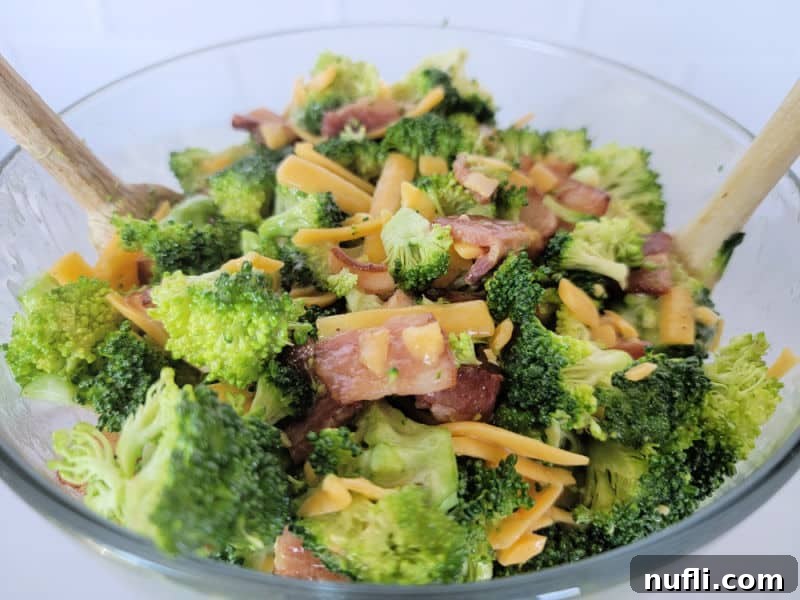 Loaded Broccoli Bacon Salad 6 Broccoli bacon salad with cheddar cheese in a glass bowl with wooden spoons