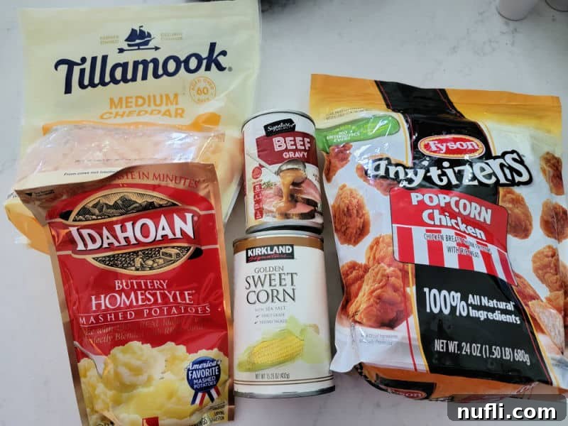 Individual ingredients for KFC Famous Bowl: Tillamook cheddar cheese, Idahoan Mashed potatoes, canned corn, beef gravy, and Tyson popcorn chicken arranged on a white kitchen counter.