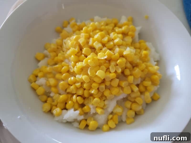 Golden sweet corn kernels spread over a bed of mashed potatoes in a white bowl.