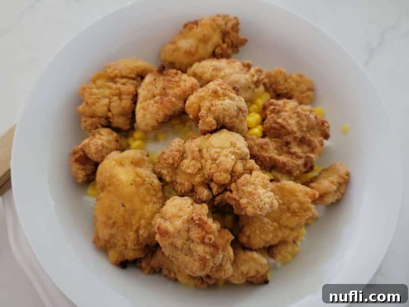 Crispy golden popcorn chicken pieces layered on top of sweet corn and mashed potatoes in a white bowl.