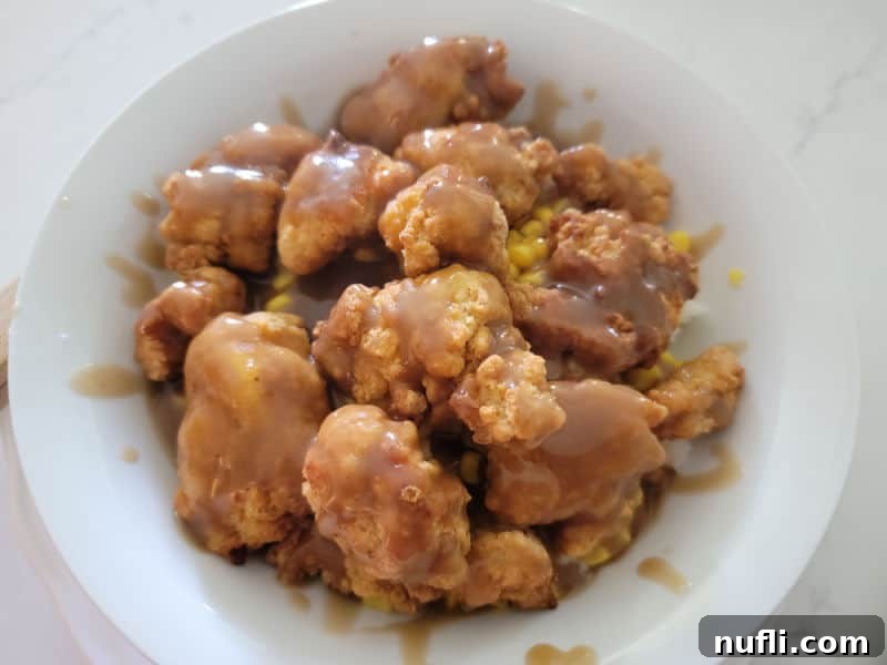 Savory beef gravy generously drizzled over crispy chicken and sweet corn in a white bowl.