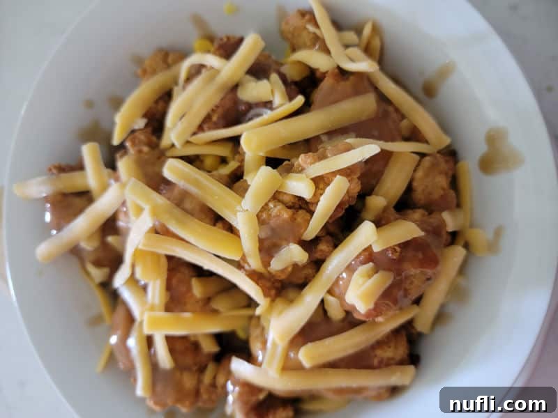 Shredded cheddar cheese sprinkled over the gravy and chicken, ready to melt.