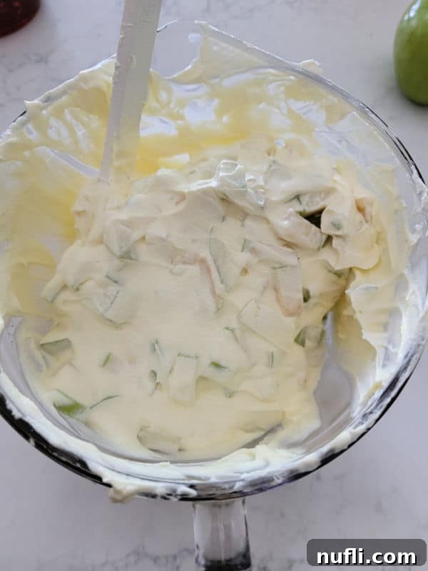 Cool whip and pudding mixed with diced apples in a glass bowl