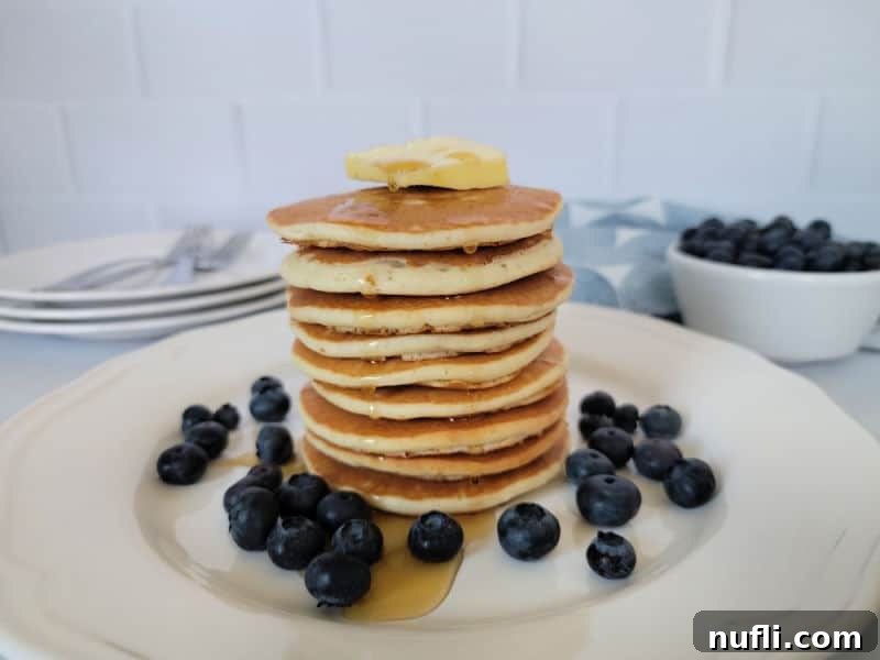 Stack of pancakes on a white plate with syrup and blueberries