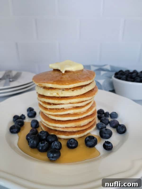 Stack of pancakes on a white plate with syrup and blueberries