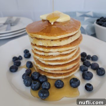 stack of air fried pancakes on a white plate with syrup, butter, and blueberries