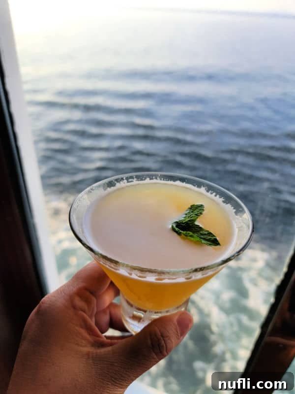 Sweet Heat Chipotle Pineapple Martini 3 Hand holding a spicy chipotle pineapple martini with the ocean in the background
