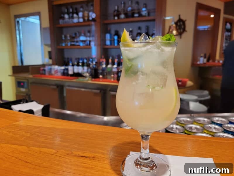 The Ultimate Carnival Cruise Ting Mojito 6 A Ting Mojito in a hurricane glass on a napkin, with blurred glasses and a bar background.