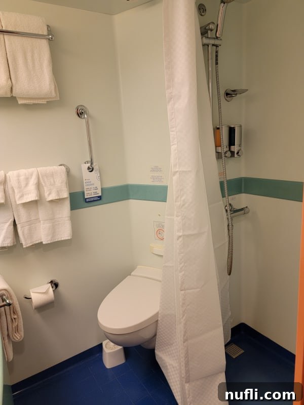 Cruise bathroom with white shower curtain, toilet, and towels attached to the wall