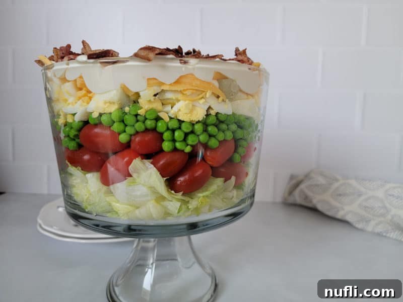Traditional 7 layer salad in a trifle dish on a white counter with a cloth napkin behind. 