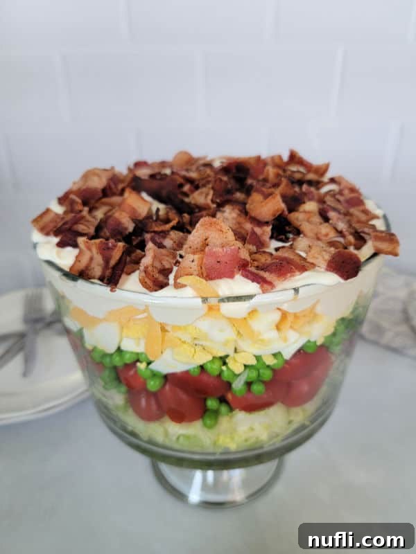 7 layer salad in a trifle bowl with bacon on top, on a white counter. 